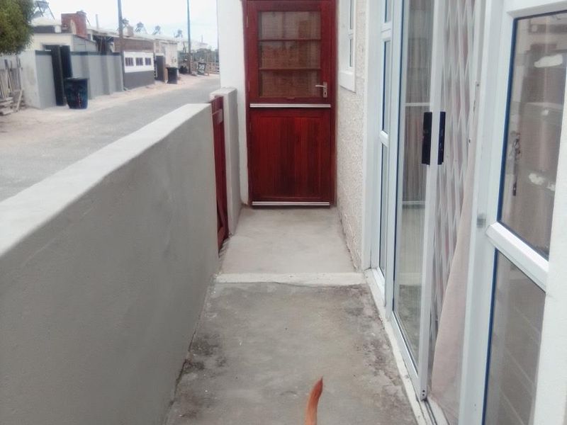 A narrow exterior side passage featuring a solid timber stable-style door, concrete flooring, and sliding glass door access to the main dwelling.