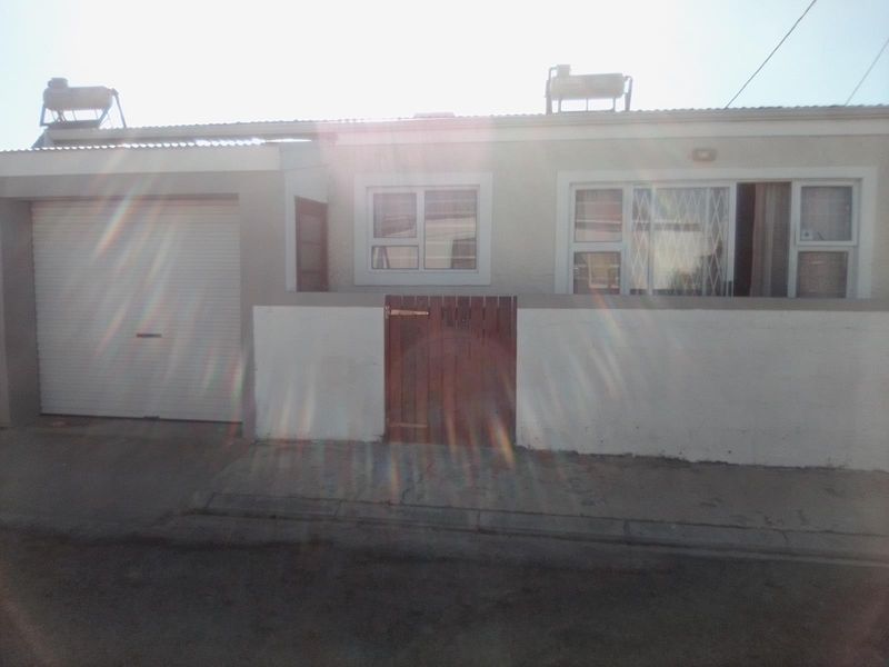 Front exterior view of a single-story house featuring a garage, secure pedestrian gate, and solar water heating systems installed on the roof.