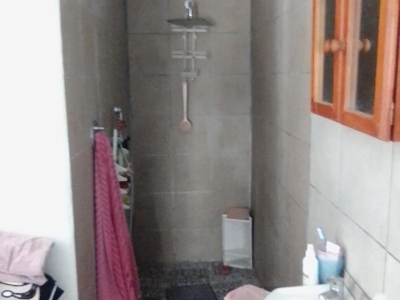 A compact bathroom featuring a shower area with tiled walls, a wall-mounted vanity cabinet, and a pedestal sink.