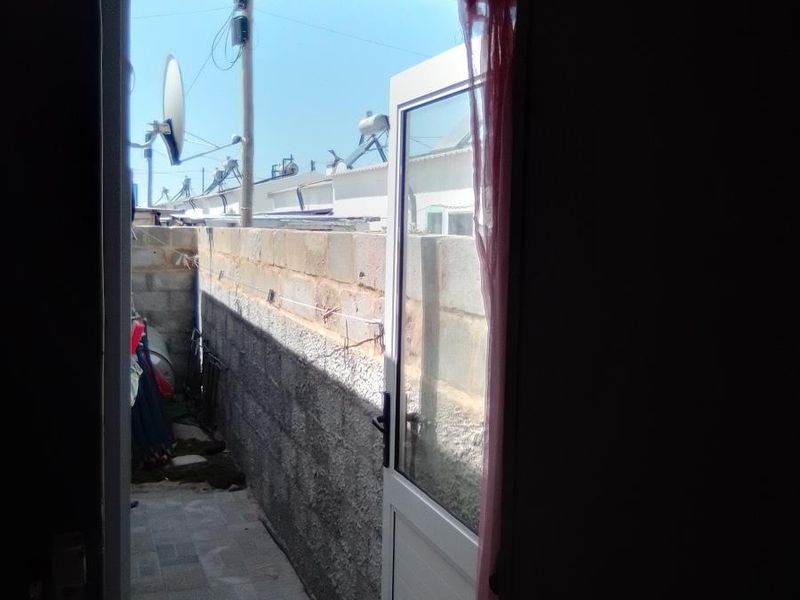 A view through an open door leading to a narrow, paved outdoor side passage enclosed by unfinished concrete block walls.