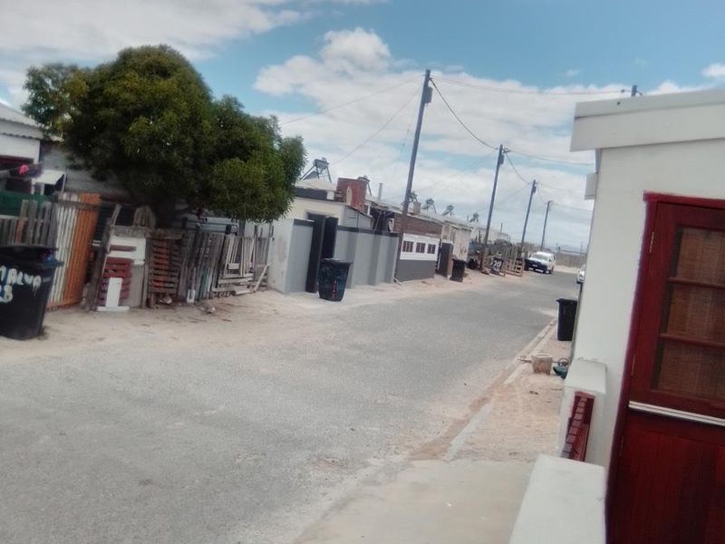 A street view showing the neighbourhood approach with unpaved road surfaces and varied boundary fencing along the residential properties.