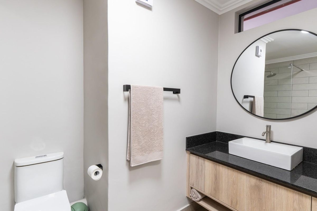 Modern bathroom featuring a floating wood-finish vanity with a black granite countertop, vessel sink, and a circular wall-mounted mirror.