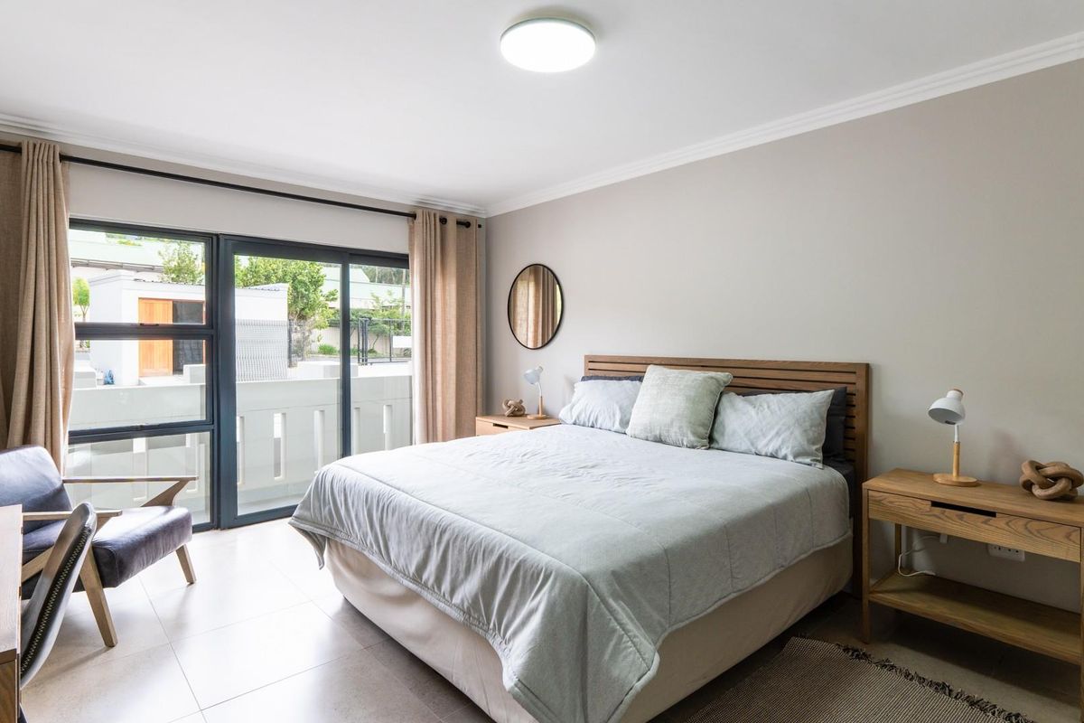 A bright and spacious bedroom featuring tiled flooring, crown molding, and large sliding glass doors that open onto a private balcony.