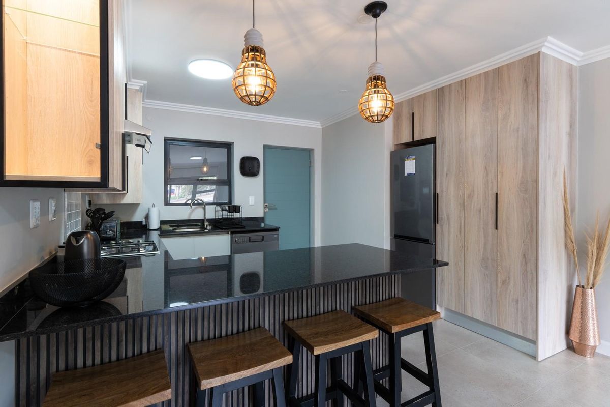 Modern kitchen featuring sleek cabinetry, dark granite countertops, a breakfast bar, and integrated storage solutions in a contemporary open-plan layout.