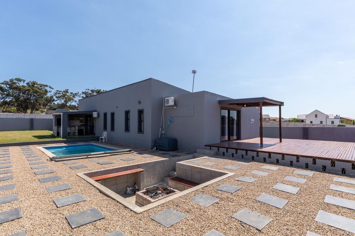Rear exterior view featuring a swimming pool, sunken fire pit area, wooden deck, and a covered patio space.