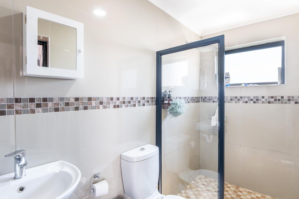 A modern bathroom featuring a glass-enclosed shower, wall-mounted vanity cabinet, and neutral wall tiling with a decorative mosaic border.