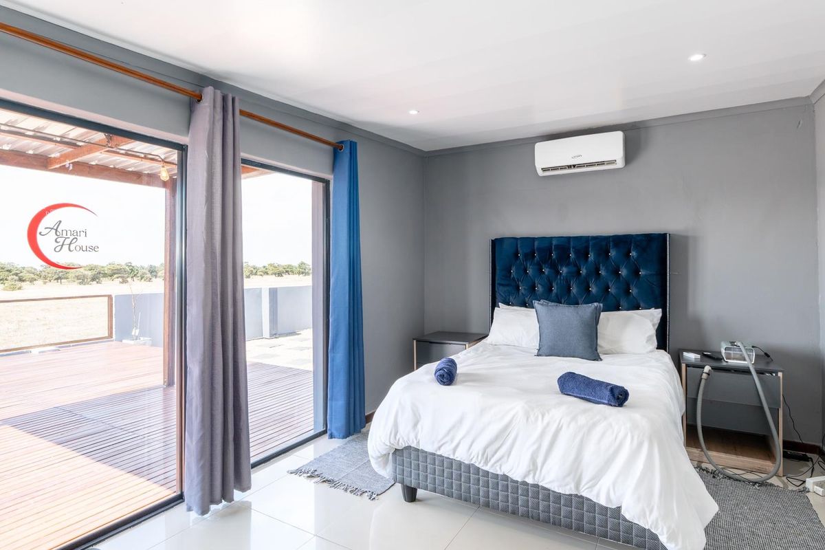 A well-maintained bedroom featuring tiled flooring, a wall-mounted air conditioning unit, and large sliding glass doors opening onto a wooden deck.