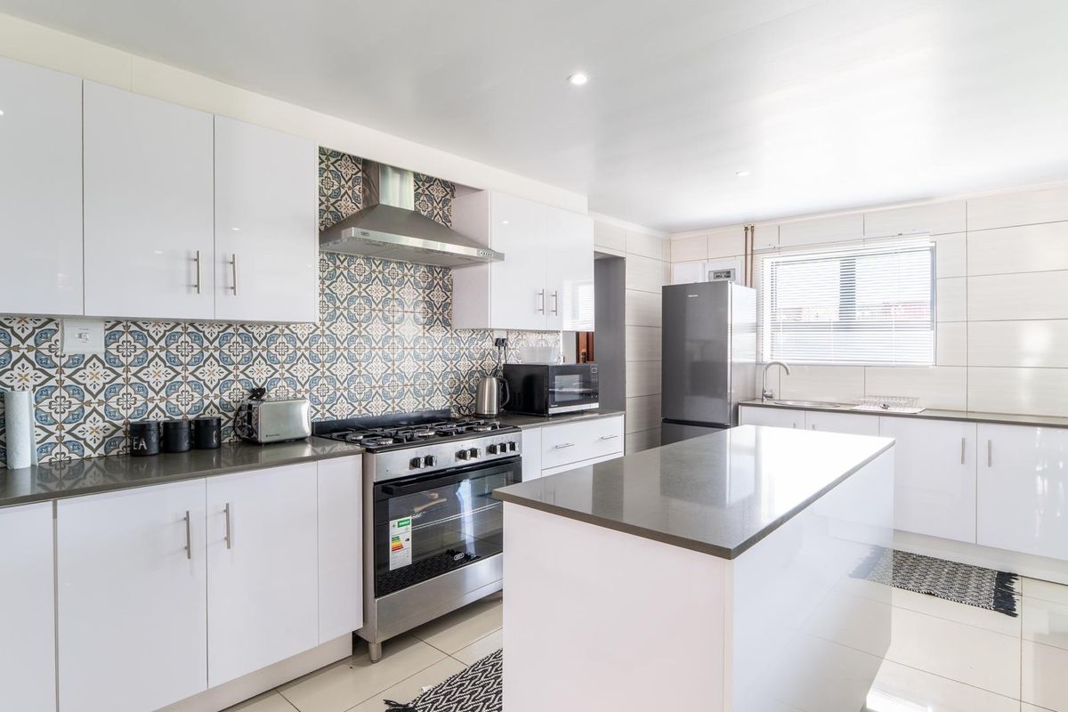 Modern kitchen featuring white cabinetry, stone countertops, a central island, patterned tile backsplash, and a stainless steel gas stove with extractor fan.
