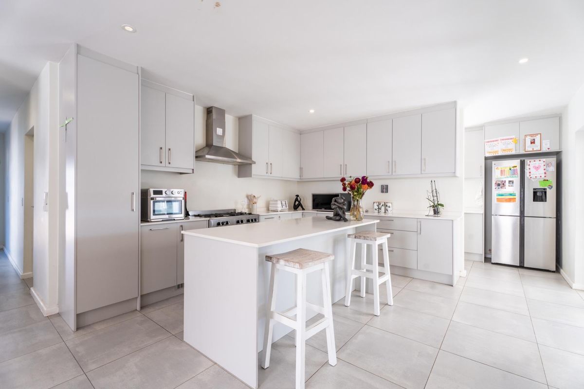 Modern kitchen featuring light grey cabinetry, stone countertops, a central island with breakfast bar seating, and stainless steel appliances.