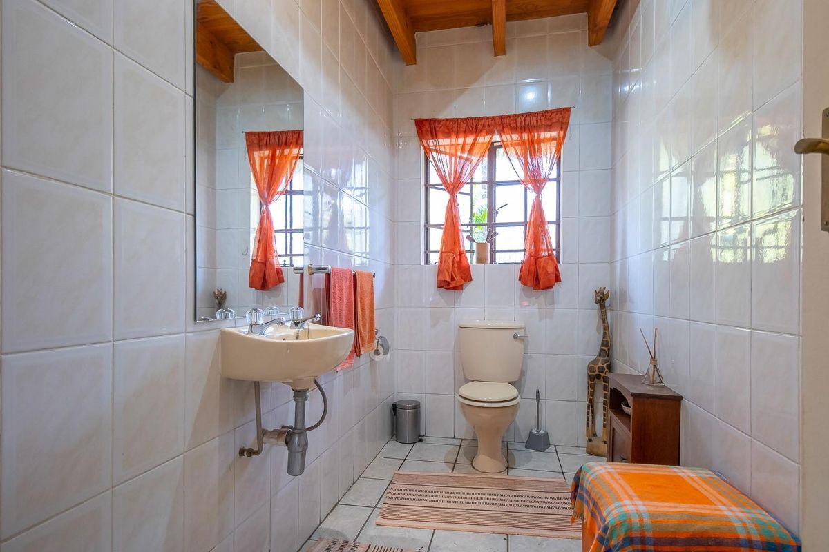 A functional bathroom featuring full-height wall tiling, a wall-mounted basin, a standard toilet, and exposed timber ceiling beams.