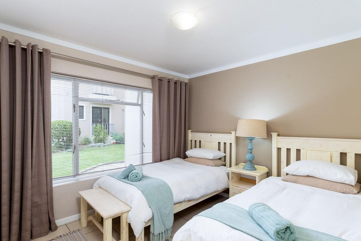 A well-maintained bedroom featuring tiled flooring, neutral wall tones, and a large window with integrated blinds overlooking the garden area.