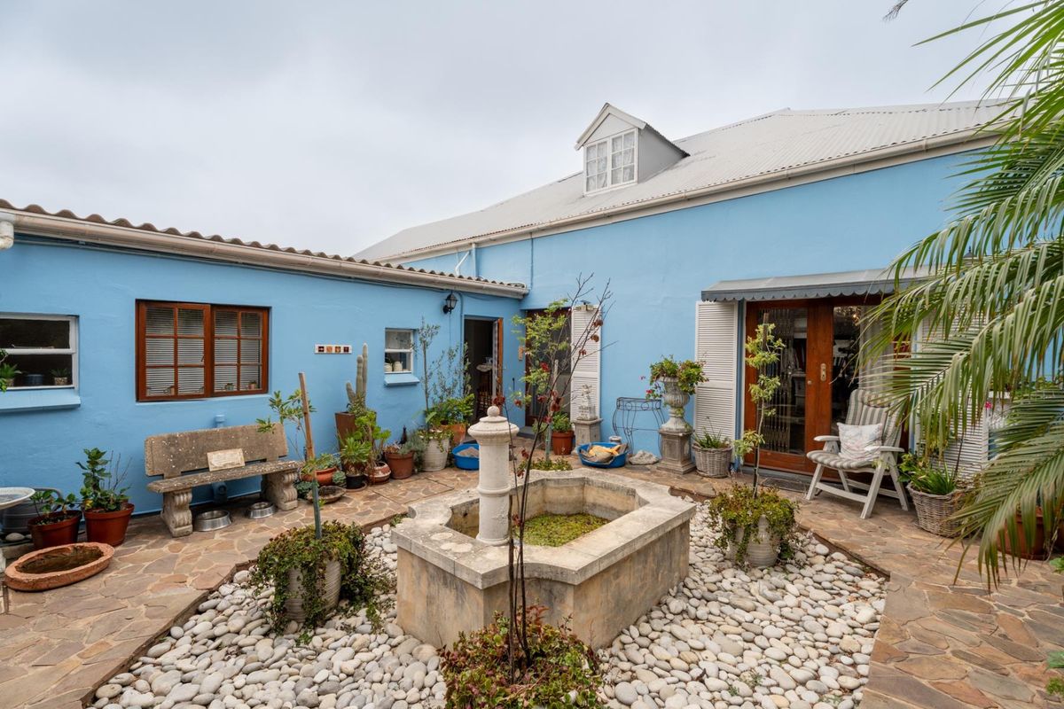 A charming enclosed courtyard featuring a central stone fountain, stone-paved flooring, and blue-painted exterior walls with access to the main dwelling.