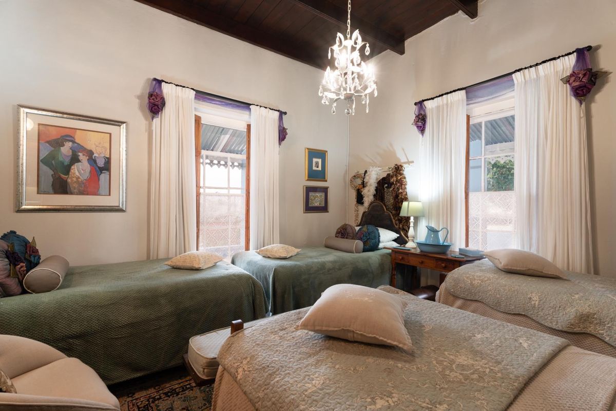 A spacious bedroom featuring high exposed timber beam ceilings, large windows, and a classic chandelier, offering a bright and character-filled living space.