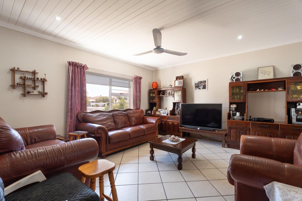 A spacious living room featuring tiled flooring, a white tongue-and-groove ceiling, and a ceiling fan, offering a comfortable and functional living space.