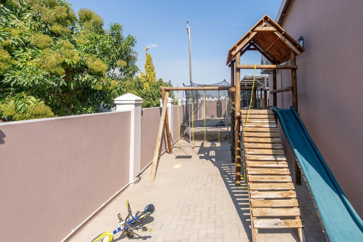 A paved side yard area featuring a perimeter boundary wall and a wooden children's play structure with a slide.
