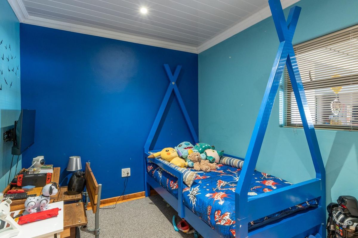 A bedroom featuring blue painted walls, a white tongue-and-groove ceiling, and a window with fitted blinds.