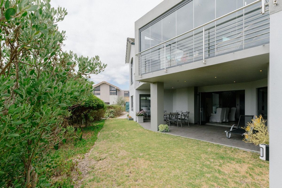 A well-maintained rear exterior featuring a covered patio area, a spacious upper balcony with glass balustrades, and a neat garden lawn.