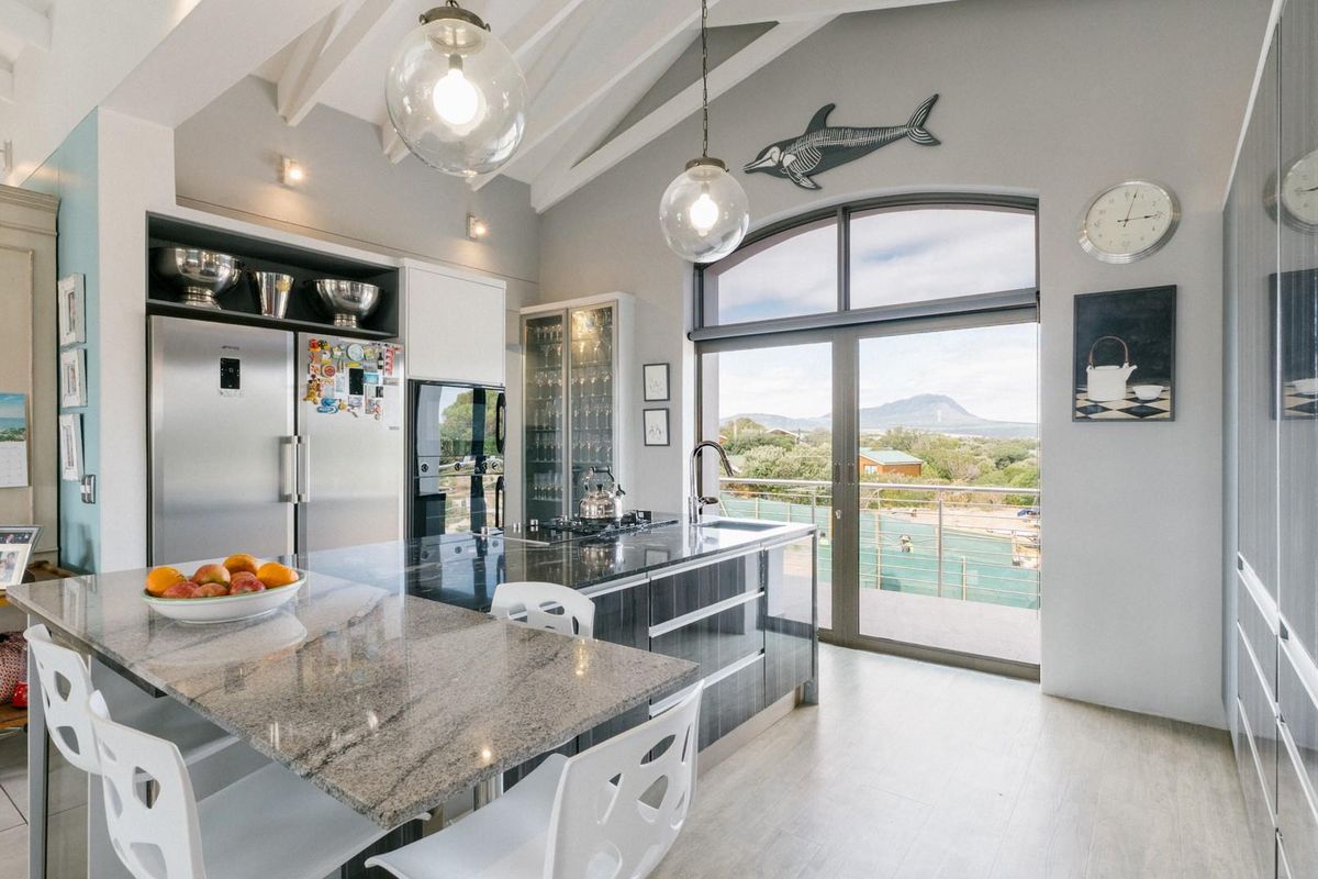 Modern kitchen featuring granite countertops, high-end cabinetry, vaulted ceilings, and large sliding doors opening to a scenic balcony view.