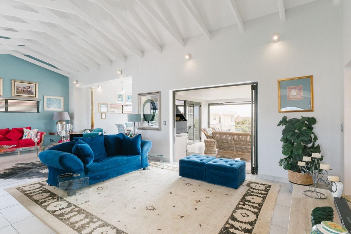 Spacious living room featuring a high vaulted ceiling with exposed beams, tiled flooring, and bi-fold doors leading to an outdoor patio area.