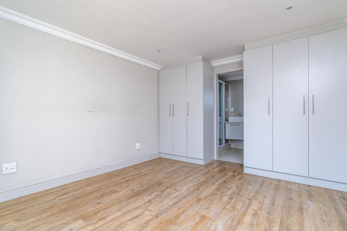A bright bedroom featuring light wood-look flooring, built-in cupboards, and an adjoining en-suite bathroom.