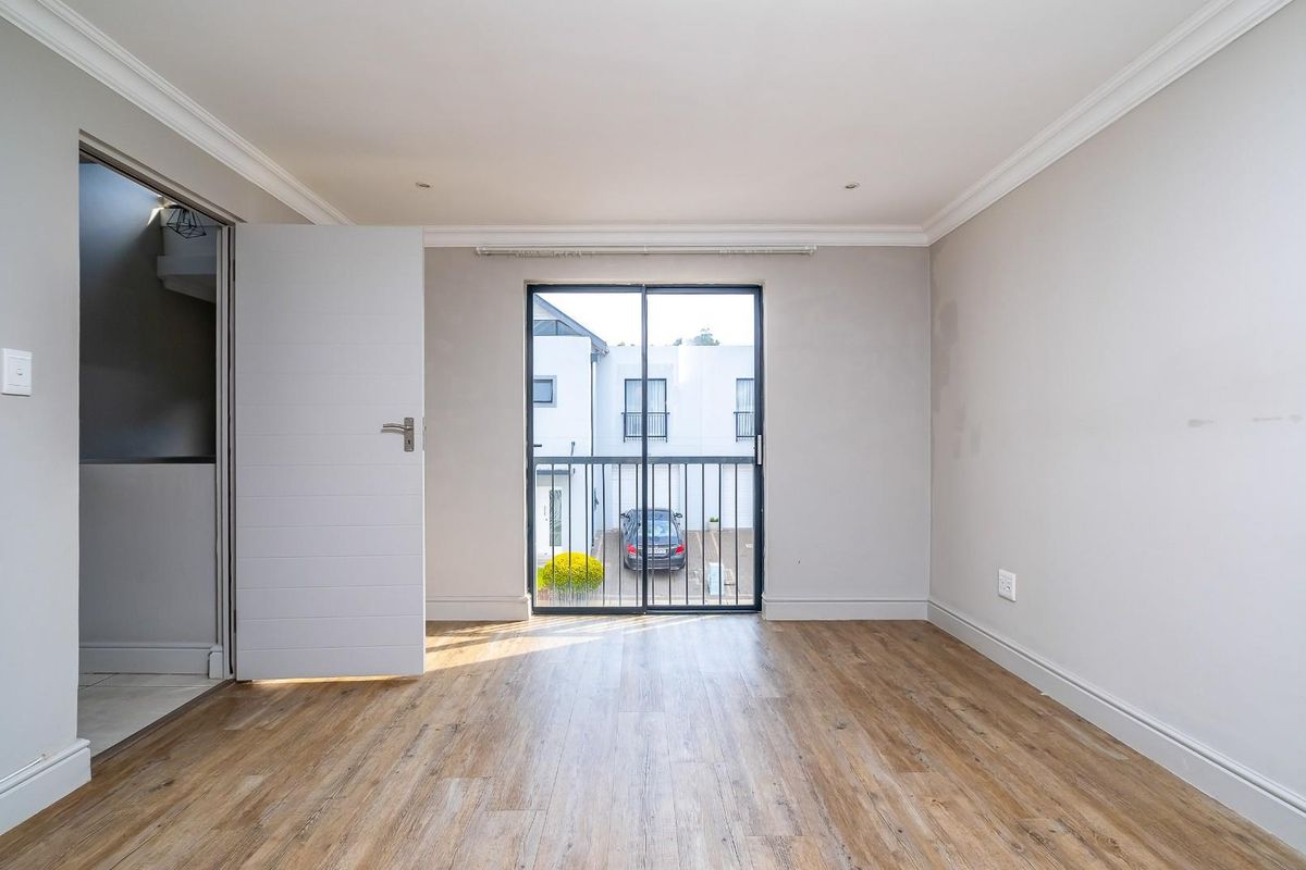 A bright, empty bedroom featuring wood-look flooring, crown molding, and a sliding glass door leading to a small balcony.