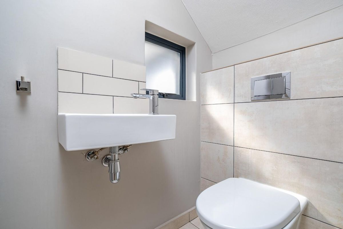 A modern guest bathroom featuring a wall-mounted basin with chrome fixtures and a concealed cistern toilet with large format wall tiles.