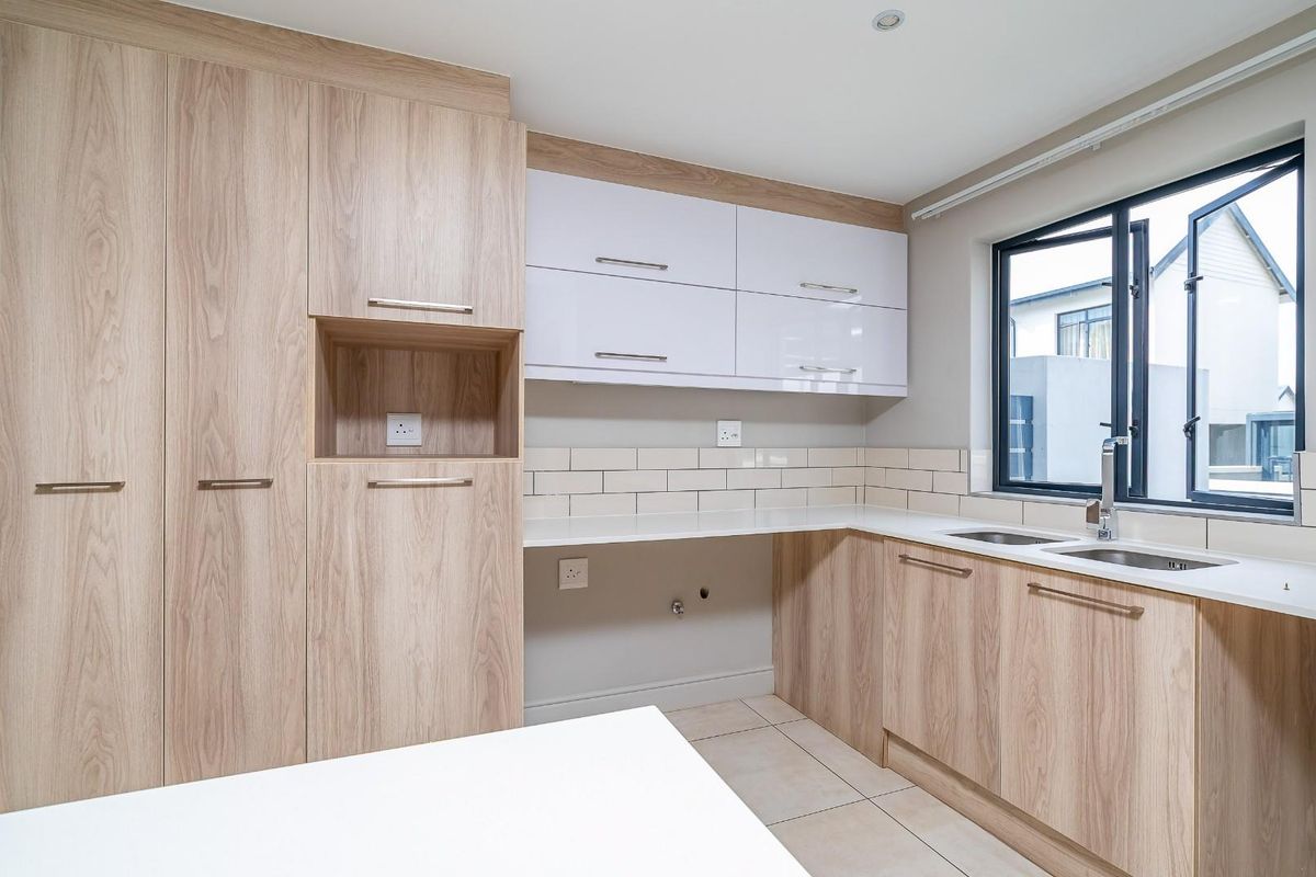 Modern kitchen featuring light wood-grain cabinetry, white high-gloss upper cabinets, subway tile backsplash, and a double-basin sink with a window view.