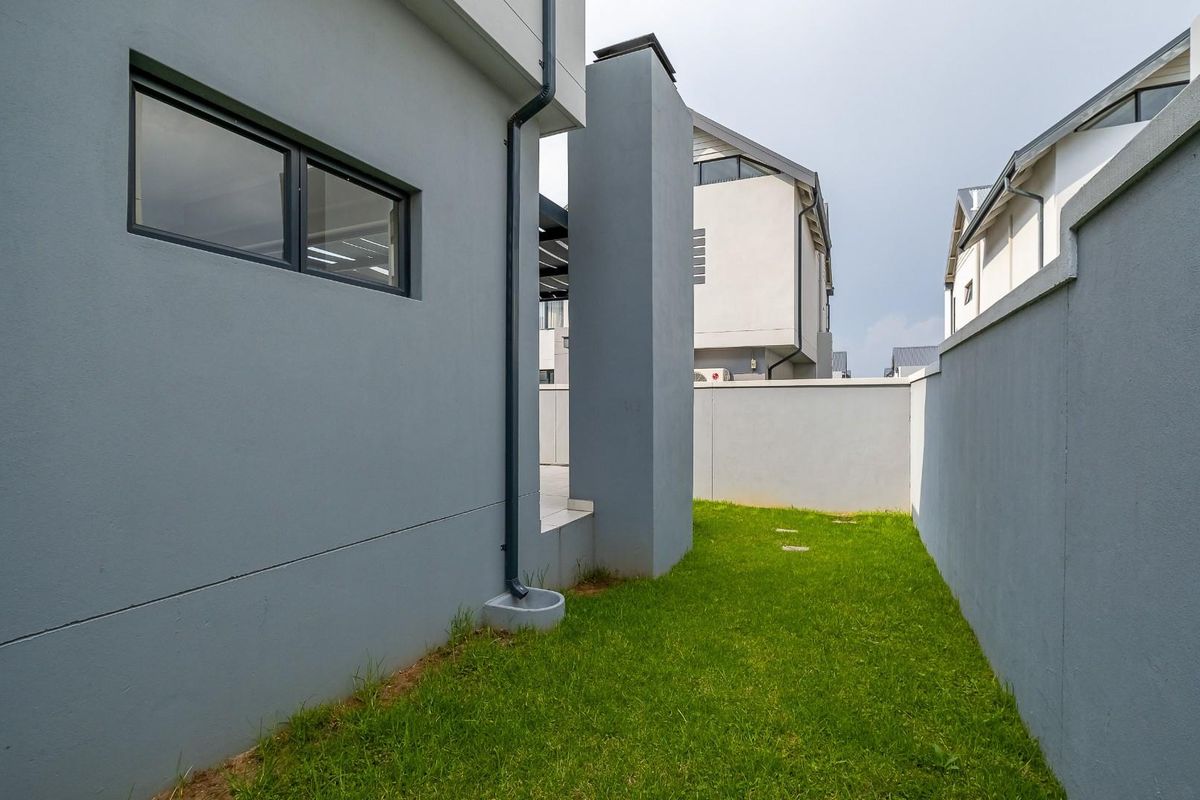 A side garden area featuring a manicured lawn, perimeter boundary walls, and modern exterior building finishes with integrated downpipes.