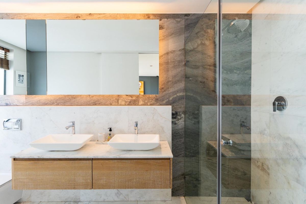Modern bathroom featuring a double vanity with vessel sinks, marble wall tiling, and a glass-enclosed walk-in shower with integrated fixtures.