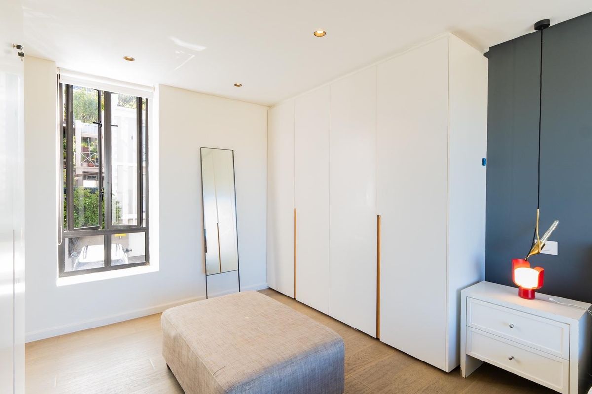 A bright bedroom featuring modern built-in floor-to-ceiling wardrobes, recessed downlighting, and light wood-look flooring.