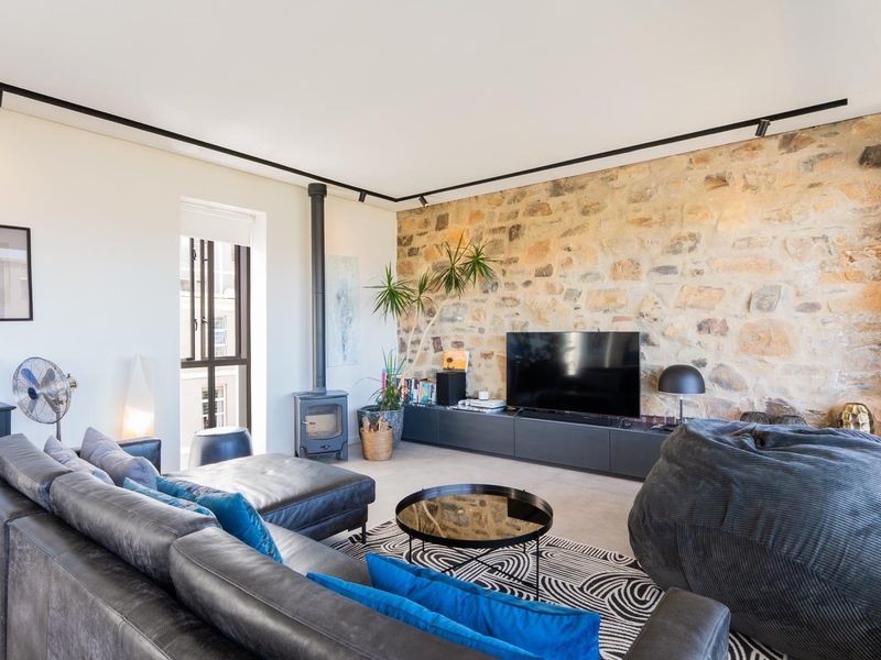 Spacious living room featuring a striking natural stone feature wall, modern track lighting, and a built-in wood-burning fireplace.