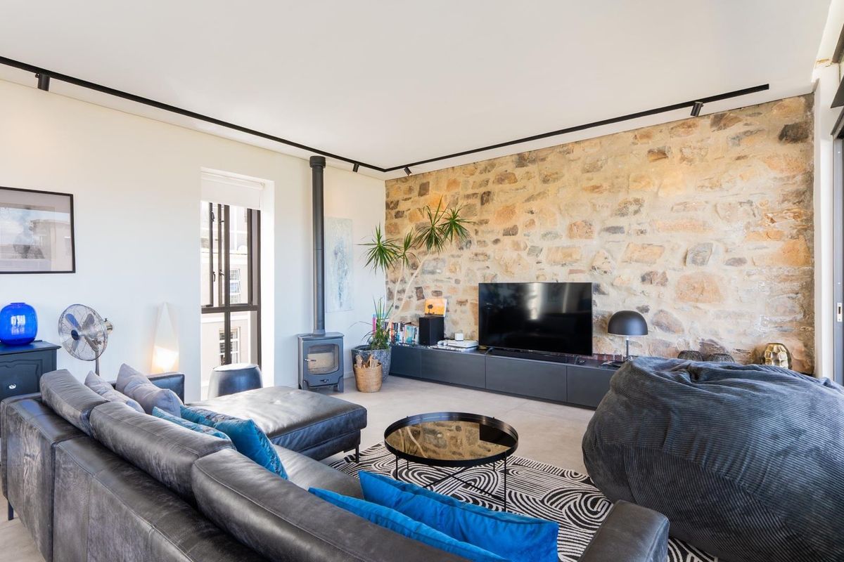 Spacious living room featuring a striking natural stone feature wall, modern track lighting, and a built-in wood-burning fireplace.