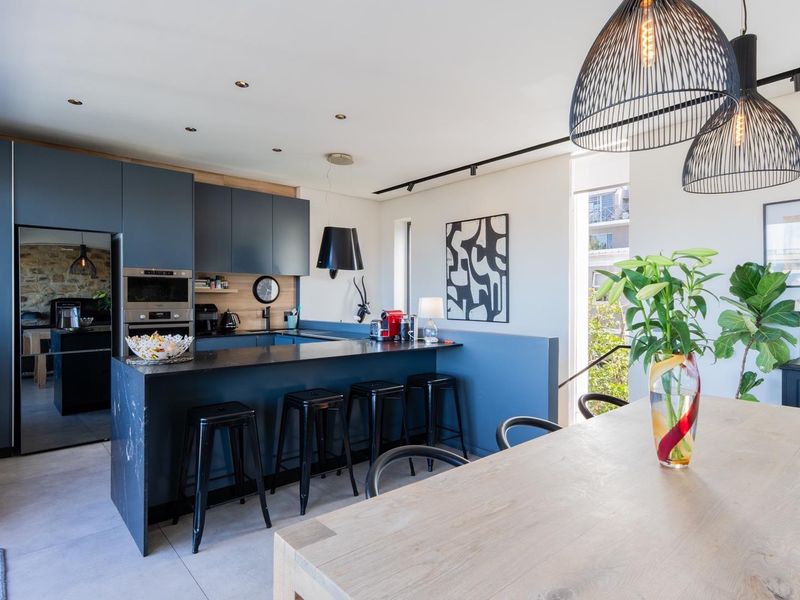 Modern open-plan kitchen featuring dark cabinetry, stone countertops, a breakfast bar, and integrated appliances, seamlessly flowing into the dining area.