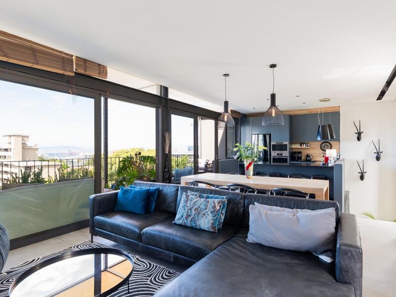 Modern open-plan living area featuring a sleek kitchen with dark cabinetry, integrated appliances, and large sliding glass doors opening to a balcony with views.