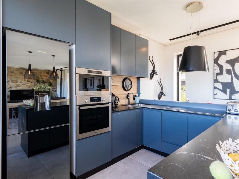 Modern kitchen featuring dark blue cabinetry, integrated stainless steel oven and microwave, black stone countertops, and a sleek pendant extractor fan.