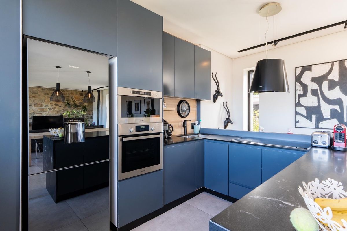 Modern kitchen featuring dark blue cabinetry, integrated stainless steel oven and microwave, black stone countertops, and a sleek pendant extractor fan.