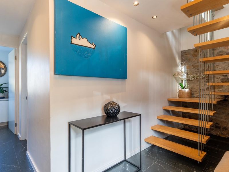Modern entrance hall featuring a floating timber staircase with metal balustrades, stone feature wall, and dark tiled flooring.
