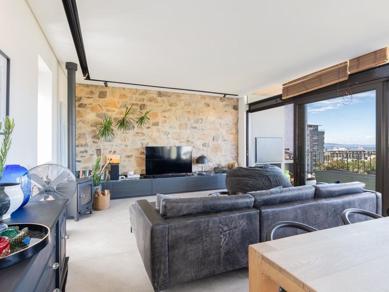Spacious open-plan living area featuring a striking natural stone feature wall, wood-burning fireplace, and large sliding doors opening to a balcony with scenic views.