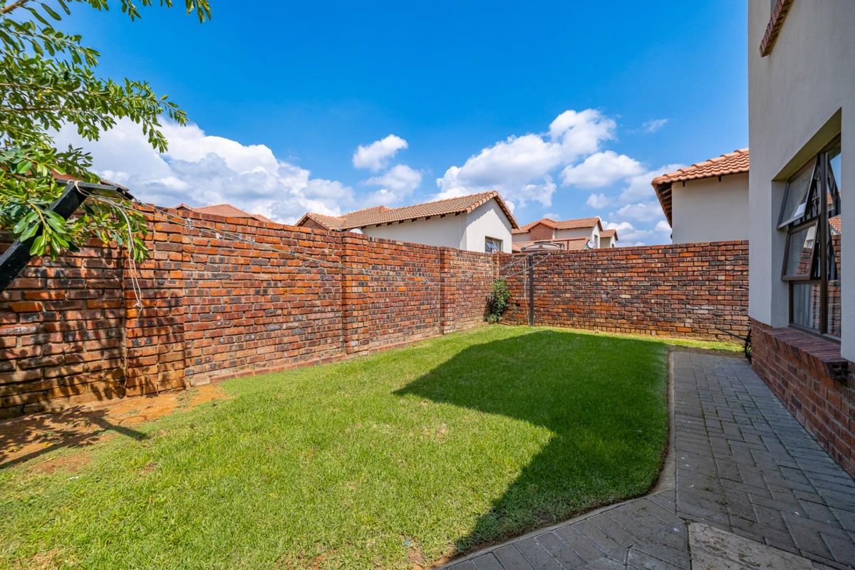 A private rear garden featuring a well-maintained lawn, paved walkway, and high perimeter face-brick boundary walls.