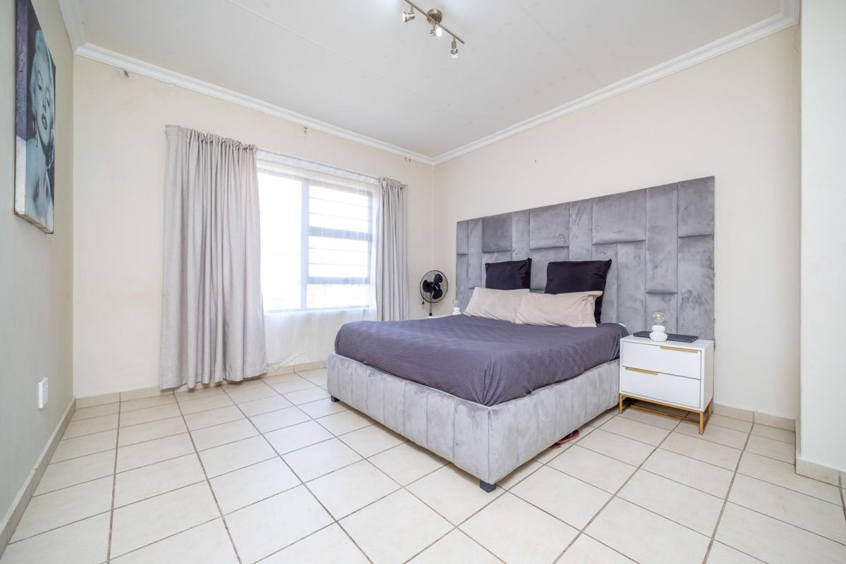 A spacious bedroom featuring tiled flooring, crown molding, and a large window with curtain tracks.