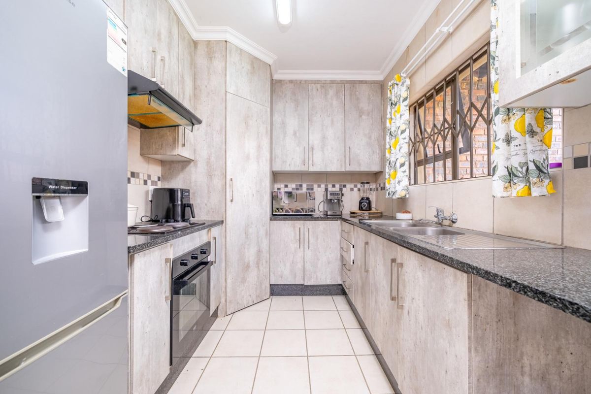 Functional kitchen featuring light wood-look cabinetry, granite countertops, a built-in oven, extractor fan, and a double stainless steel sink with security bars on windows.