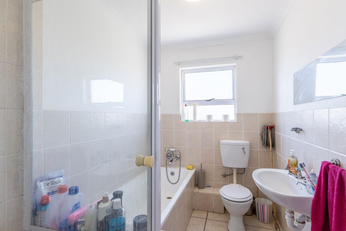 A functional bathroom featuring a bathtub with shower mixer, pedestal basin, and toilet, finished with neutral wall tiles and tiled flooring.