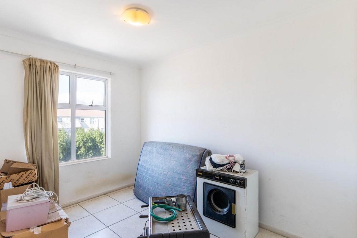 A functional bedroom featuring tiled flooring, a built-in cupboard, and a window providing natural light.