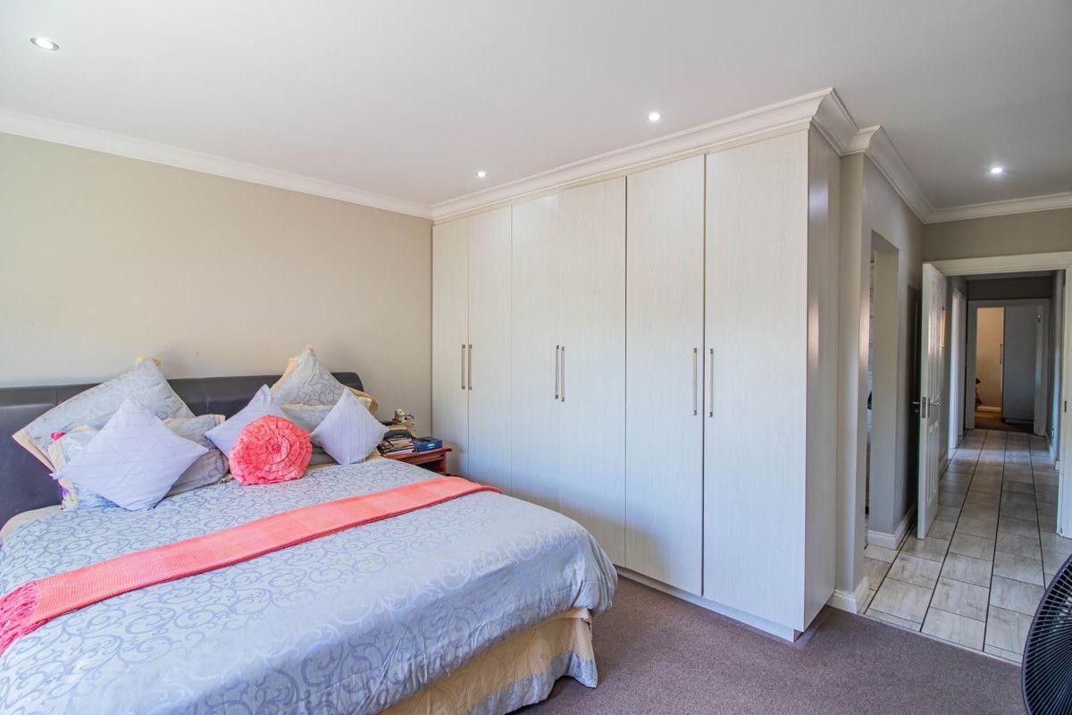 A well-maintained bedroom featuring built-in floor-to-ceiling wardrobes, recessed downlighting, and neutral carpeting, with an adjacent hallway leading to further living spaces.