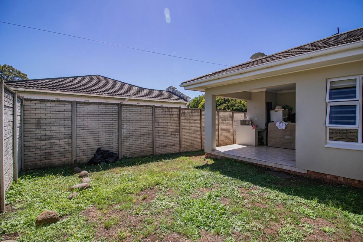 A rear view of the townhouse featuring a covered patio area with a built-in braai and a private garden enclosed by boundary walls.