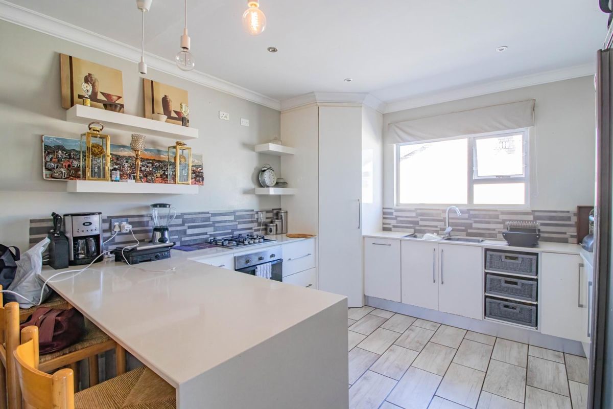 Modern kitchen featuring white cabinetry, stone countertops, a built-in oven and hob, tiled backsplash, and a breakfast bar island.