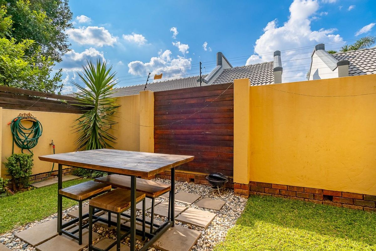 A private rear garden featuring a paved seating area, established lawn, and high boundary walls with timber feature paneling.