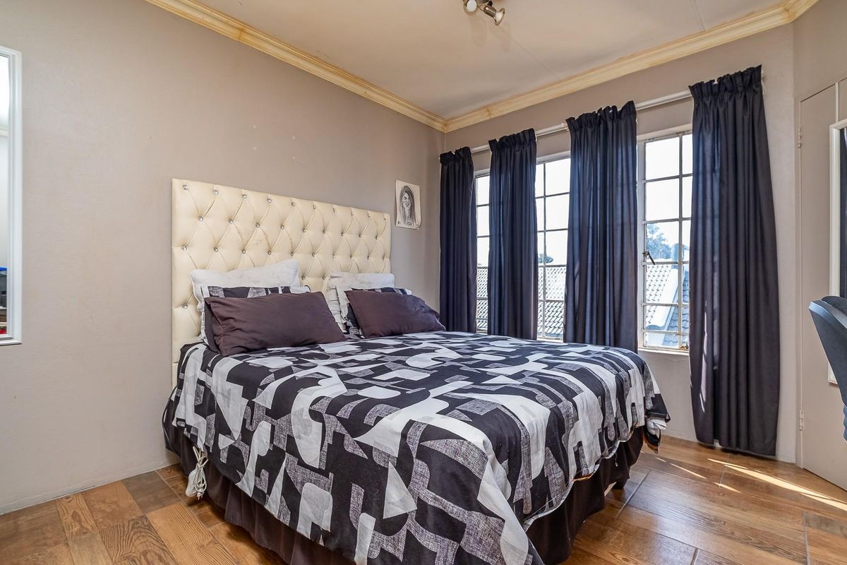 A bedroom featuring wood-look tiled flooring, crown molding, and large windows with dark curtains, providing natural light and a view of the surrounding area.