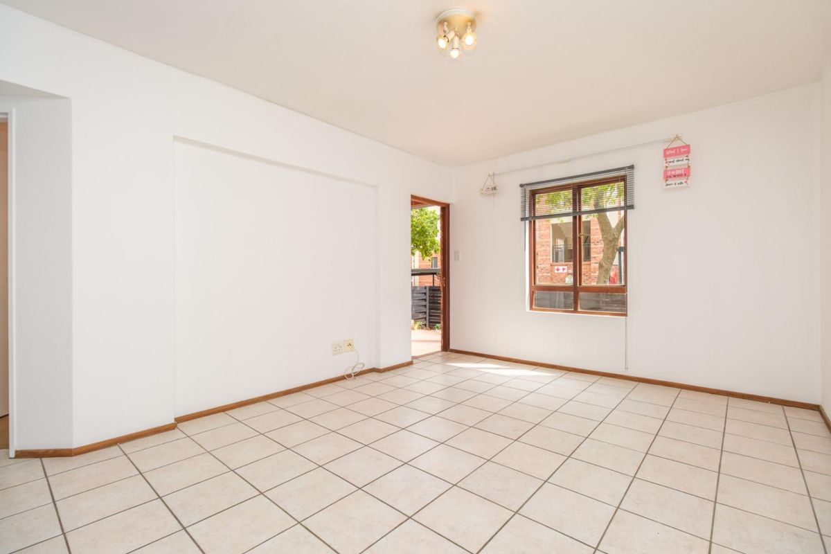 A bright, empty living area featuring neutral ceramic floor tiles, a wooden window frame, and direct access to an outdoor space.