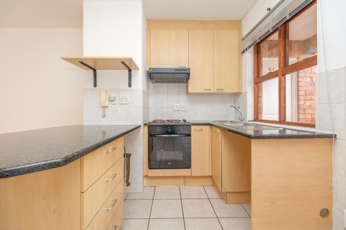 A functional kitchen featuring light wood cabinetry, dark granite countertops, a built-in oven with hob, and tiled flooring.
